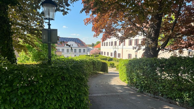 Ansicht eines Schlosses in Großrußbach, umgeben von Bäumen und Hecken, mit einer Laterne im Vordergrund.