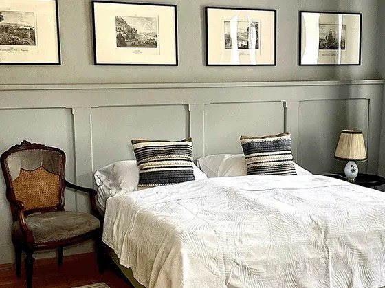 Schlafzimmer mit Doppelbett, antikem Stuhl und gerahmten Bildern an der Wand.
