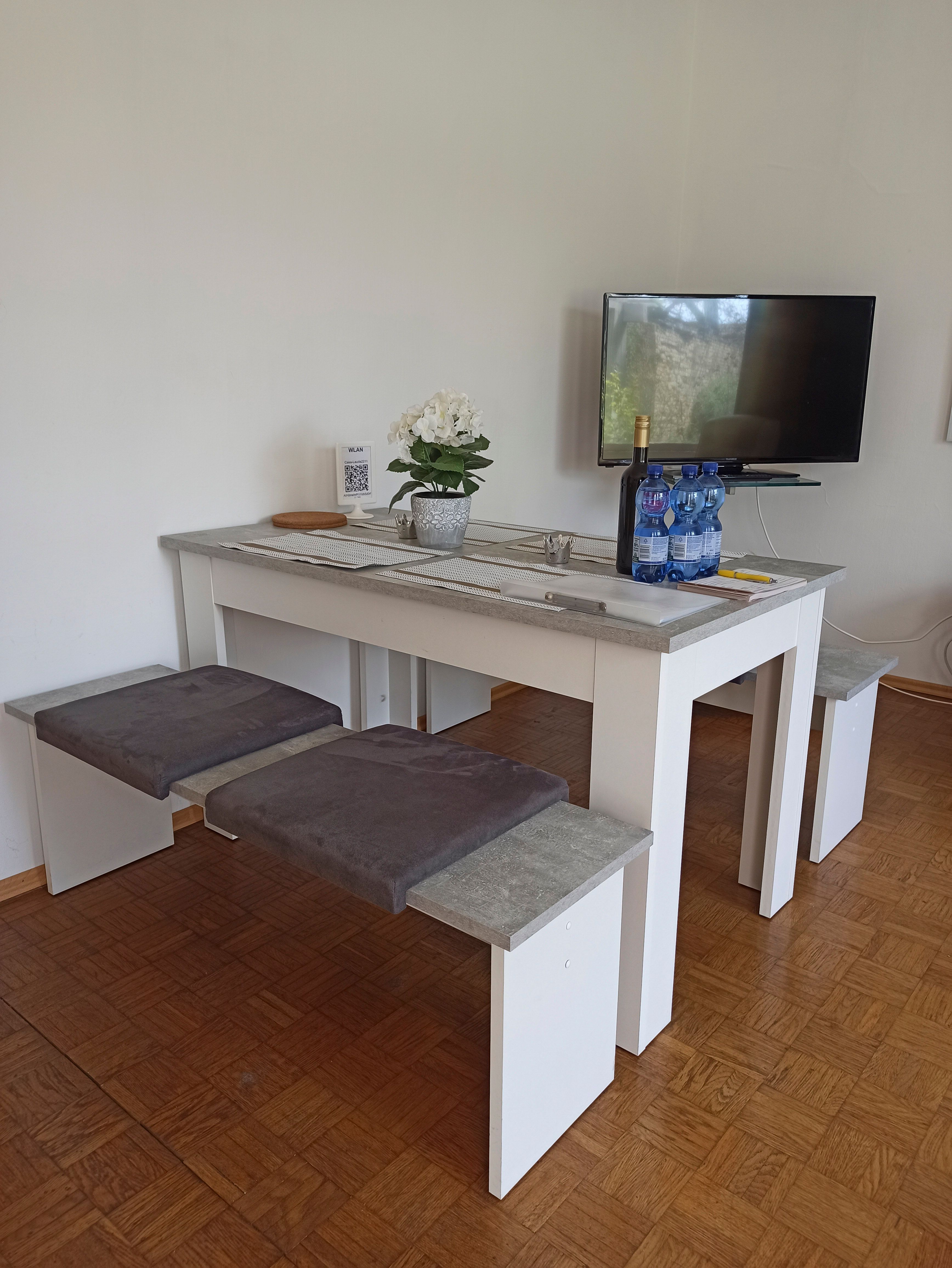 Moderner Aufenthaltsbereich mit Tisch, Bänken, Fernseher und Dekoration.