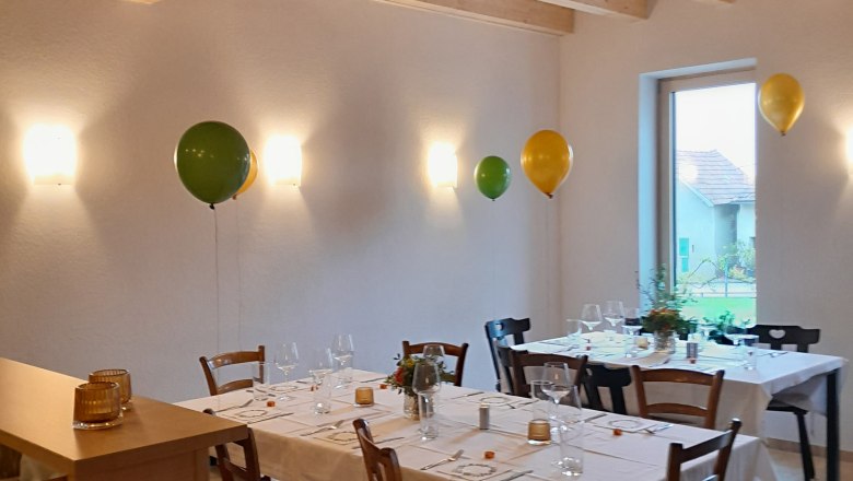 Ein festlich gedeckter Tisch in einem Raum mit Holzbalkendecke und Luftballons an der Wand.