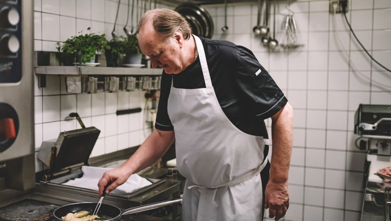 Ein Koch in einer professionellen Küche brät etwas in einer Pfanne.