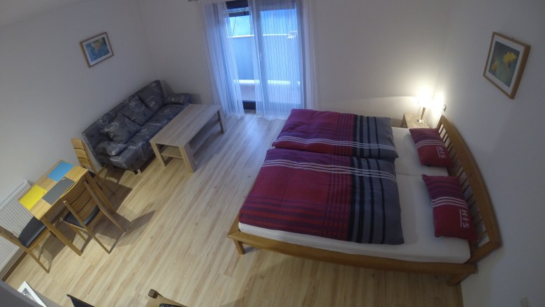 Ein einfach eingerichtetes Apartment mit Bett, Sofa, Tisch und St&uuml;hlen.