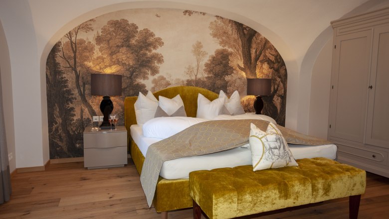 Elegante Suite mit gelbem Bett, Wandgemälde und Holzfußboden im Schloss Luberegg