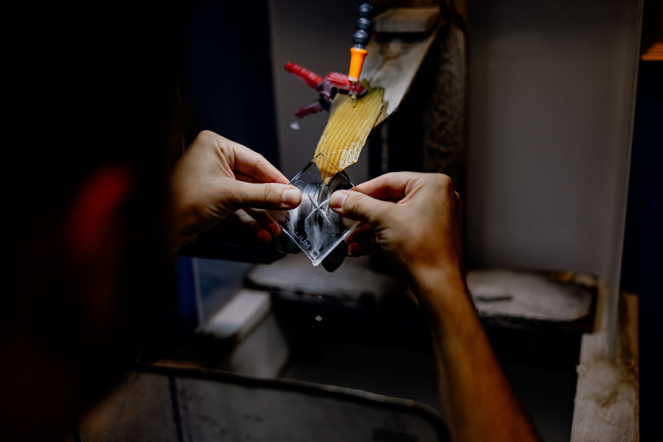 Nahaufnahme von Händen, die ein Glasstück an einer Schleifmaschine bearbeiten.