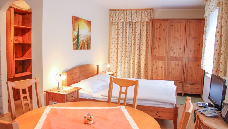 Kleine Wohnung mit Holzmöbeln, Bett, Tisch und Schrank.