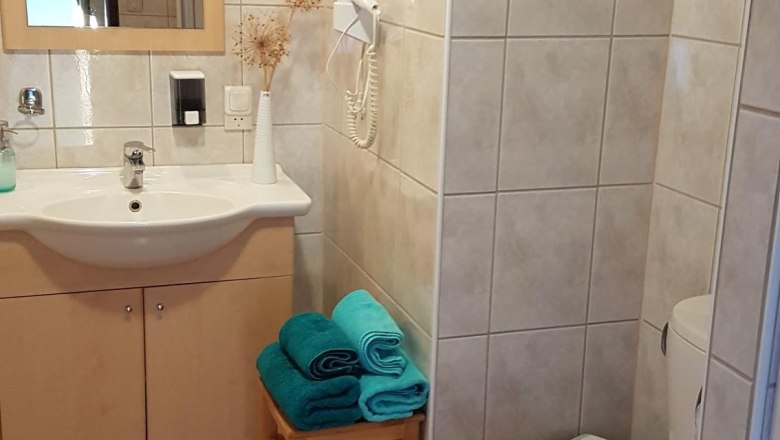 Ein Badezimmer mit Waschbecken, Spiegel, Toilette und Handt&uuml;chern auf einem Hocker.