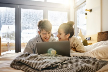 Zwei Kinder liegen auf dem Bett und schauen in den Laptop, im Hintergrund weiß Landschaft