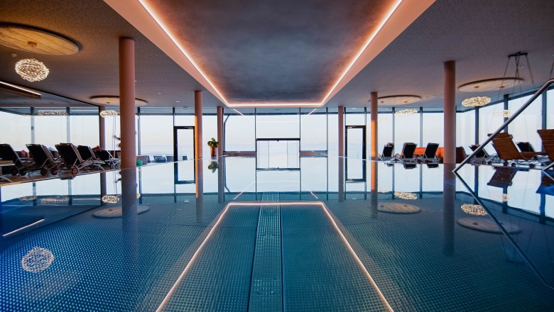 Innenansicht eines Infinitypools mit Liegestühlen und großen Fenstern.