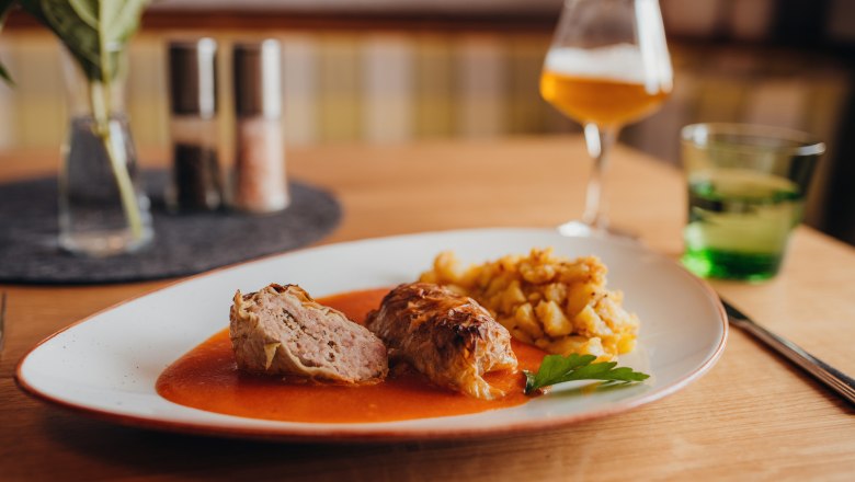 Krautroulade mit Soße und Kartoffelbeilage auf einem Teller serviert.