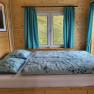 Holzinterieur mit Bett, Fenster und blauen Vorh&auml;ngen.