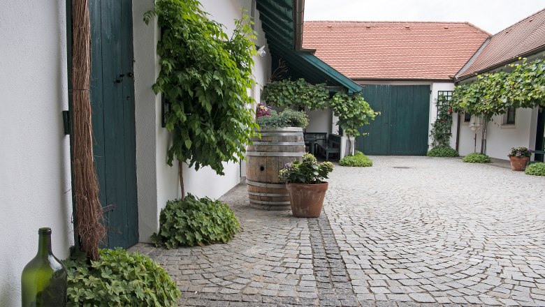 Innenhof eines Winzerhofs mit Kopfsteinpflaster, gr&uuml;nen T&uuml;ren und Pflanzen.