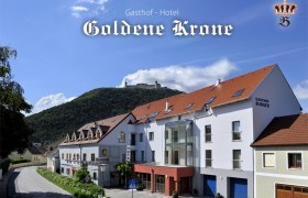 Gasthof-Hotel Goldene Krone vor einem bewaldeten Hügel mit Burg im Hintergrund.
