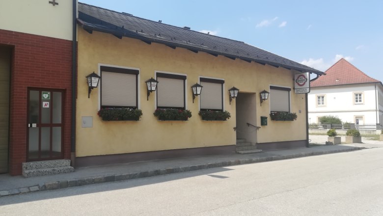 Außenansicht eines gelben Gasthauses mit geschlossenen Fensterläden und Blumenkästen.