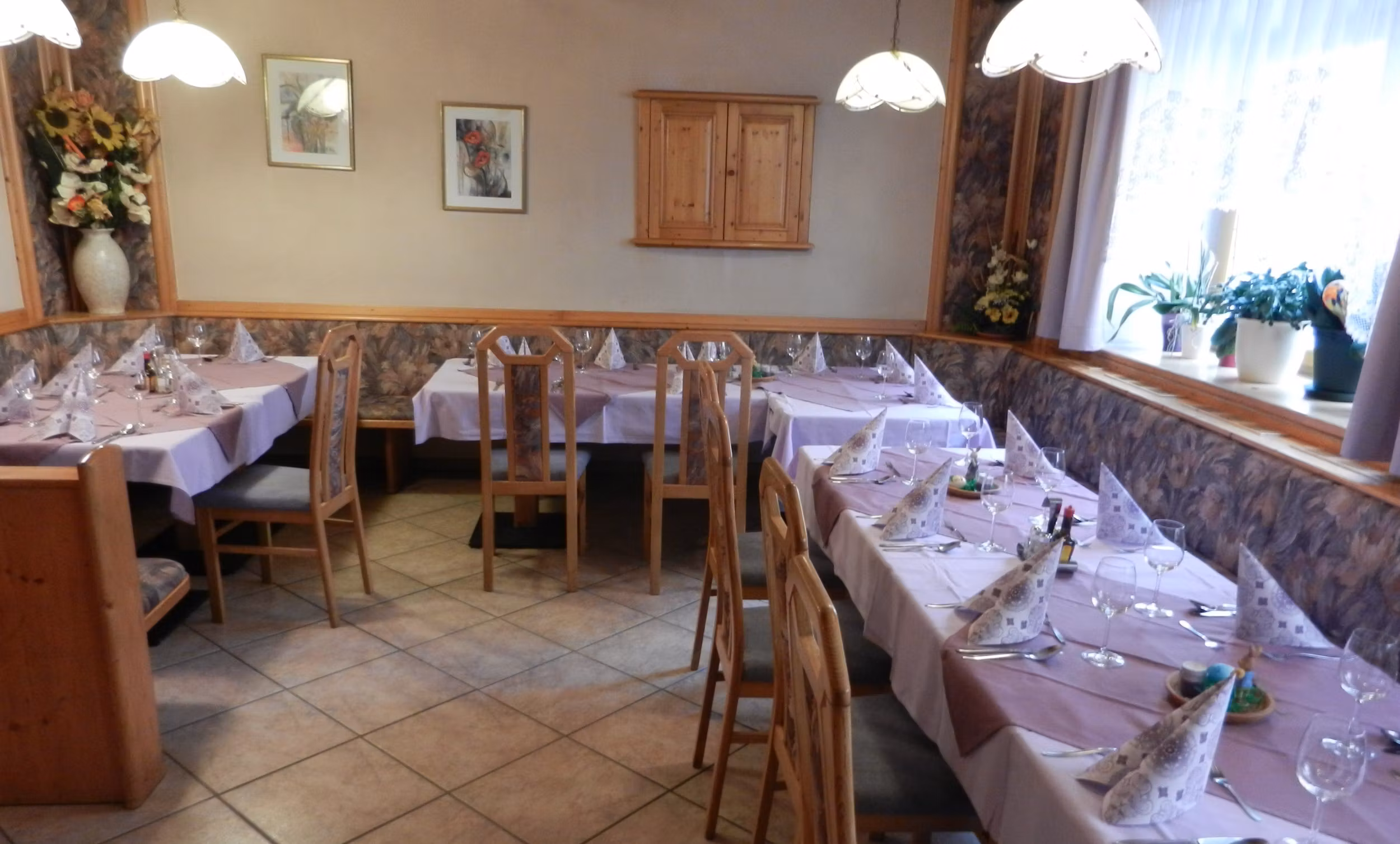 Gemütlicher Gastraum mit gedeckten Tischen und Holzstühlen.