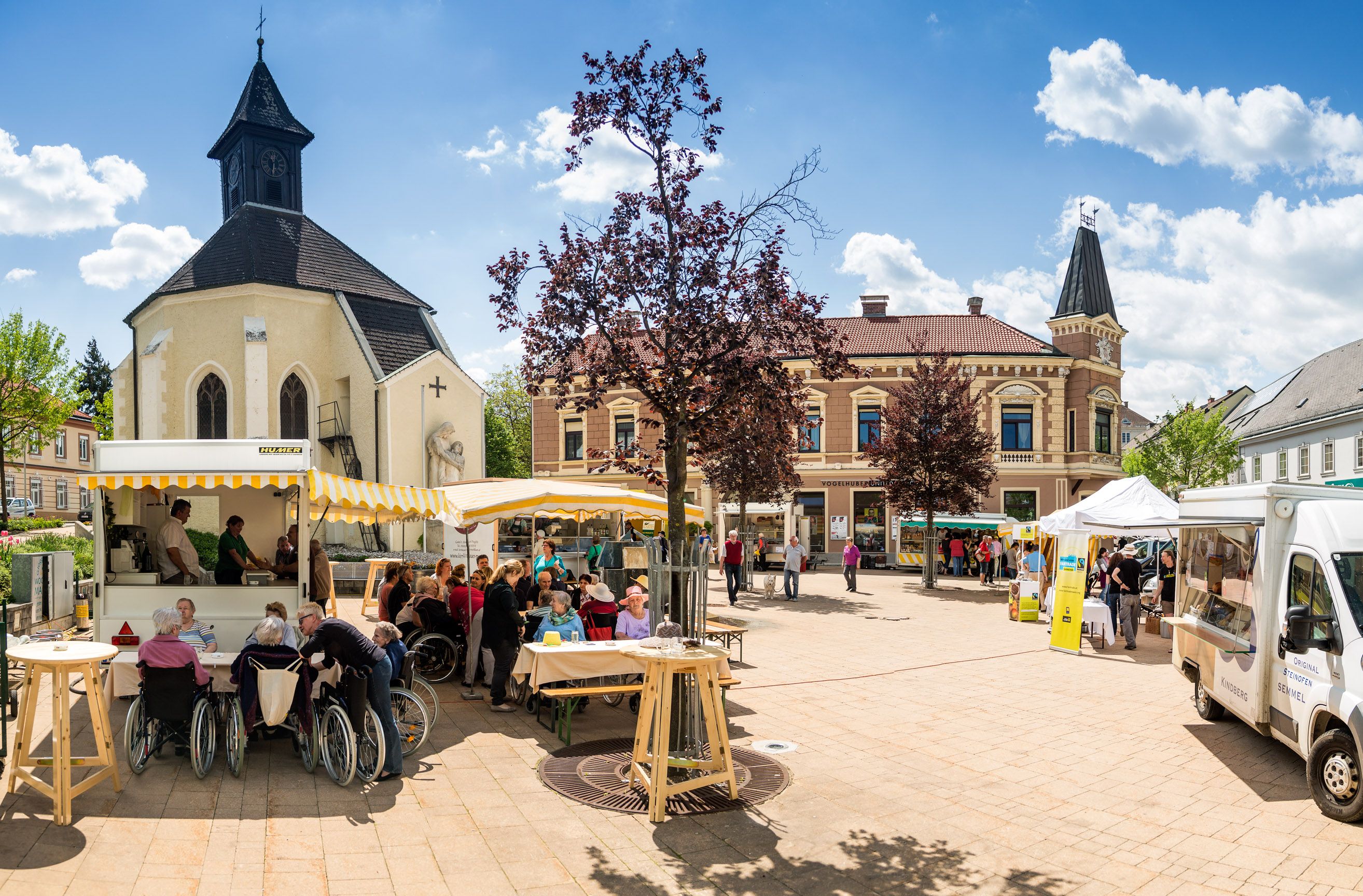 Marktplatz in Gloggnitz mit Kirche, Verkaufsständen und Menschen.