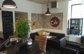 Gemütliches Café mit Pflanzen, Sitzgelegenheiten und Dekorationen.