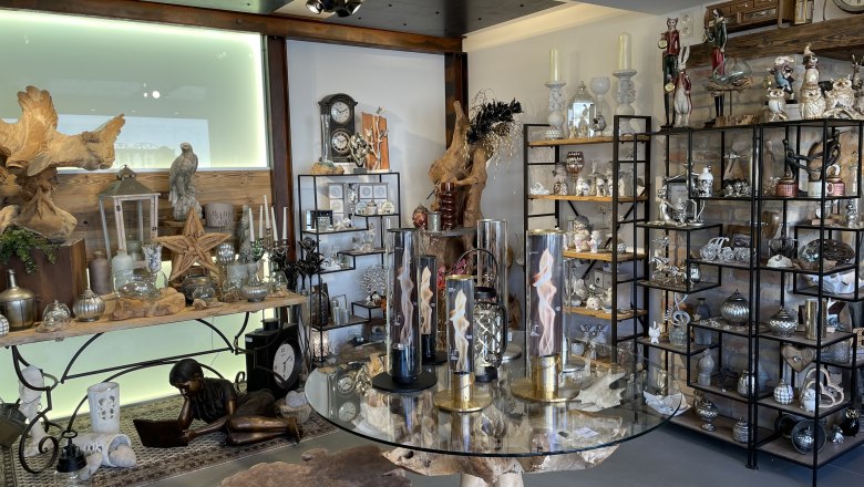 Innenansicht eines Dekorationsladens mit Regalen voller Dekoartikel und einem Tisch mit Glasplatte.