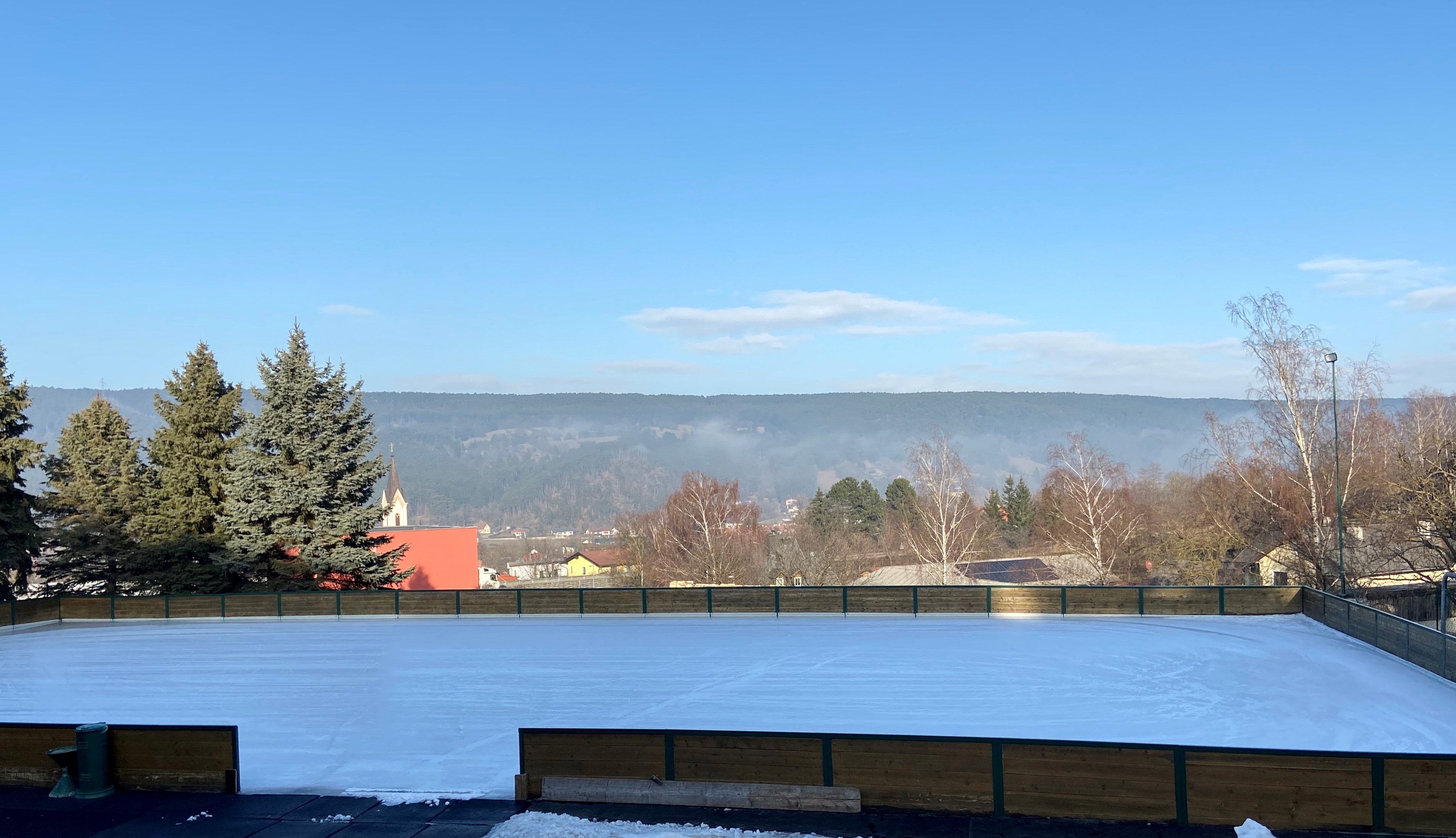 Eislaufplatz mit umliegender Landschaft und Kirche im Hintergrund.