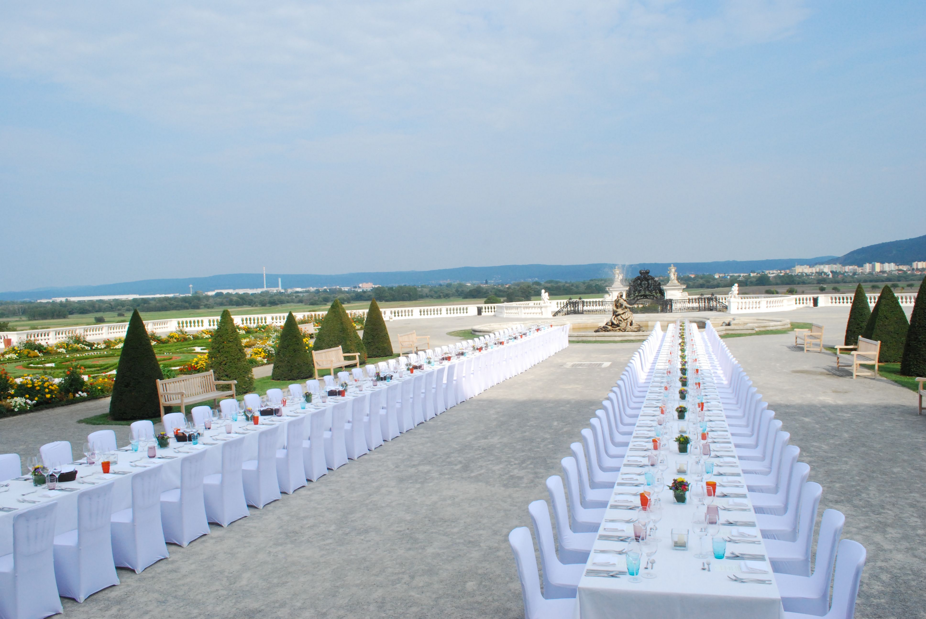 Langer, festlich gedeckter Tisch im Freien mit Blick auf einen Garten und eine Statue.