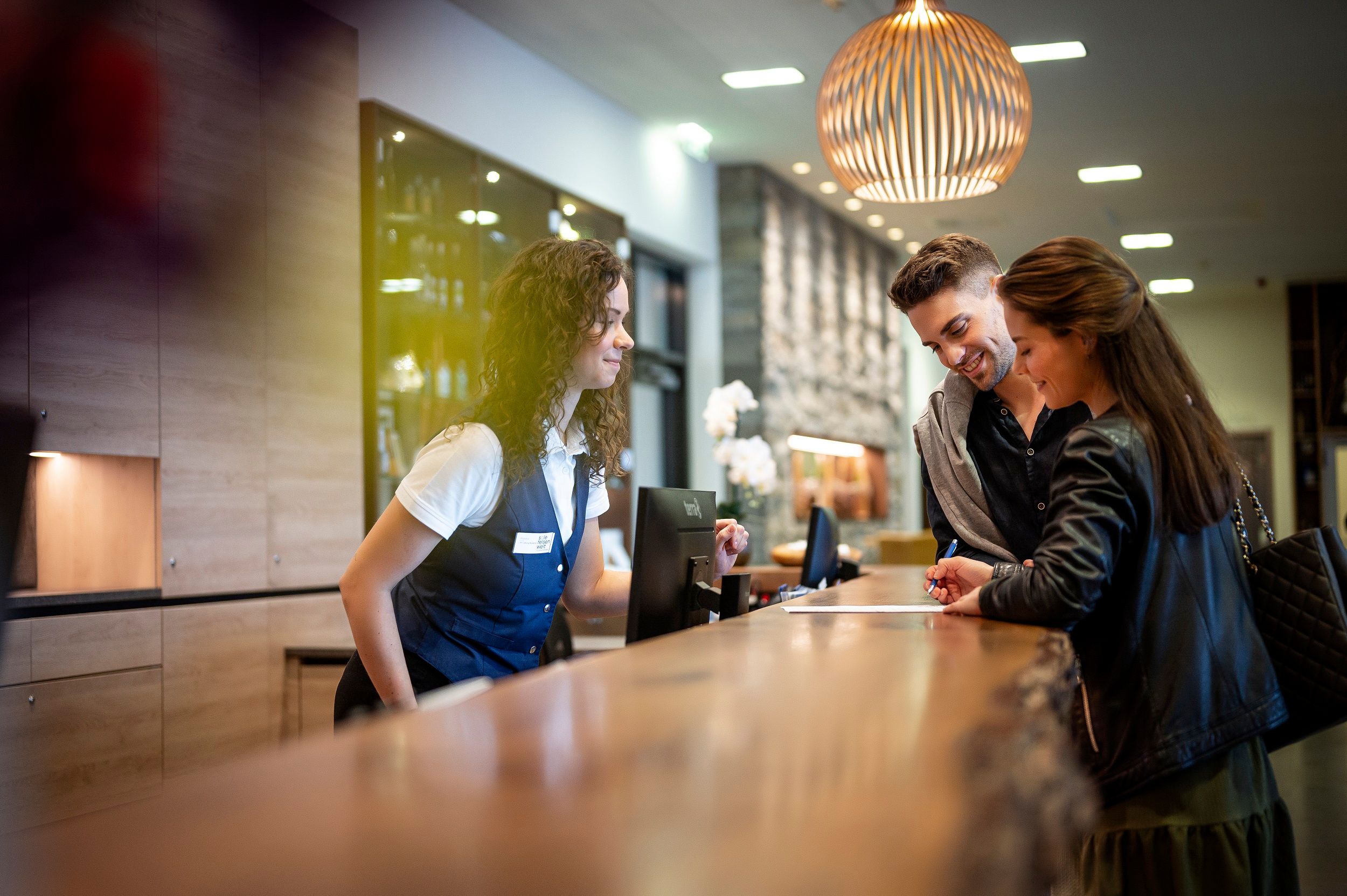 Ein Paar checkt an der Rezeption eines Hotels ein, während eine Rezeptionistin ihnen hilft.