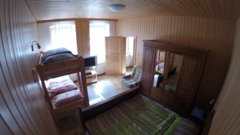 Holzvert&auml;feltes Schlafzimmer mit Etagenbett, Doppelbett, Kleiderschrank und Fernseher.