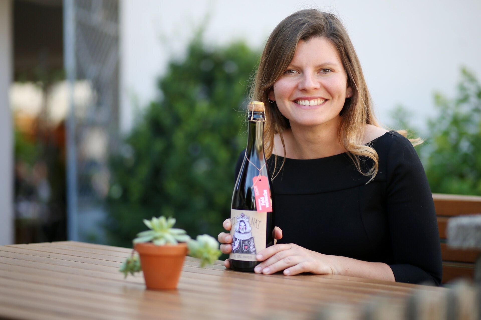 Inmitten der sanften Hügel des Mostviertels strahlt die Sonne auf eine fröhliche Frau, die stolz eine Flasche Cider präsentiert. Umgeben von üppigem Grün und blühenden Pflanzen, vermittelt die Szene ein Gefühl von Genuss und Lebensfreude, das die Schönheit der Region perfekt einfängt.