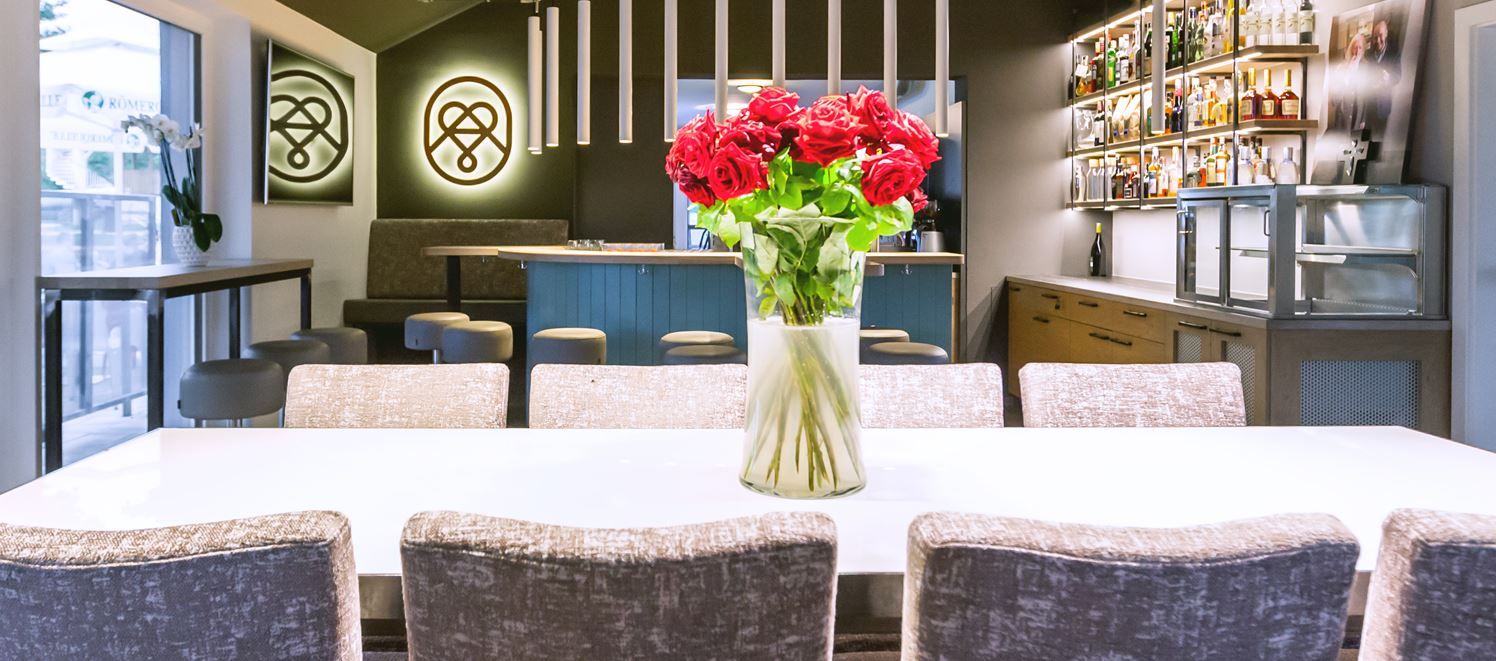 Innenansicht eines modernen Lokals mit Holztischen und Regalen; warme Beleuchtung und gemütliche Atmosphäre für Genuss und Verkostung.