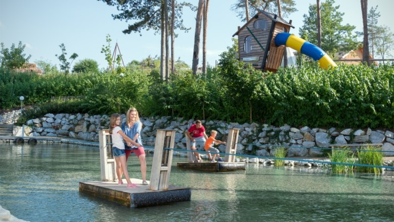 Kinder und Erwachsene fahren auf kleinen Fl&ouml;&szlig;en in einem Abenteuergarten.