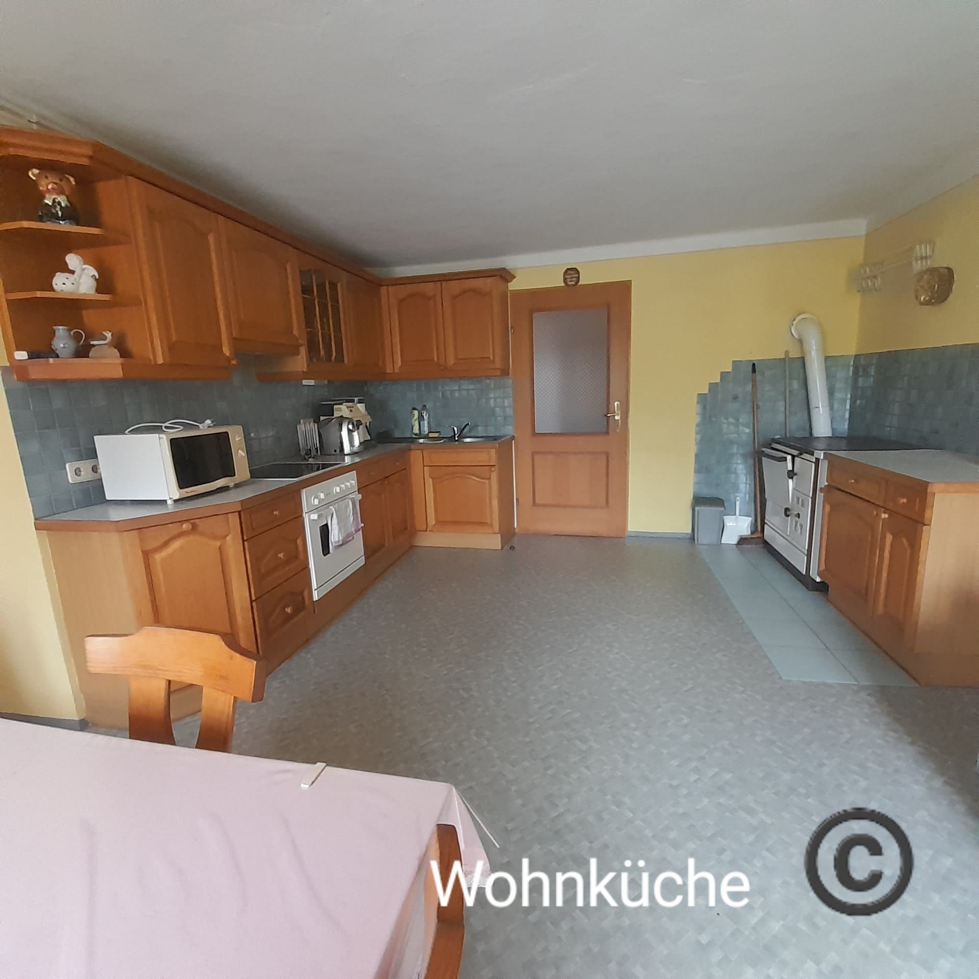 Eine geräumige Wohnküche mit Holzmöbeln, einem Esstisch, Herd, Mikrowelle und gelben Wänden.