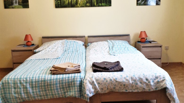 Schlafzimmer mit zwei Einzelbetten, Nachttischen und Waldlandschaftsbildern an der Wand.