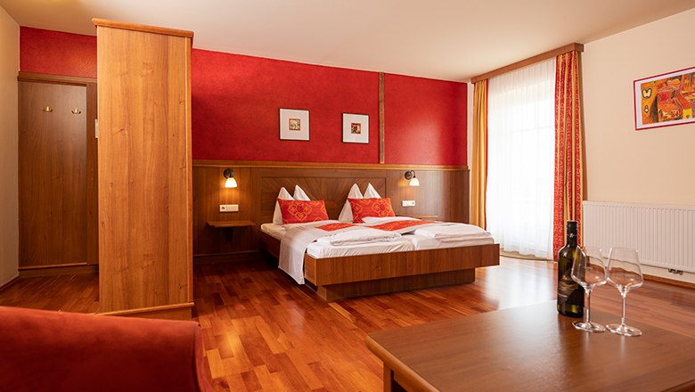 Gemütliches Hotelzimmer mit Doppelbett, Holzmöbeln und roten Akzenten.