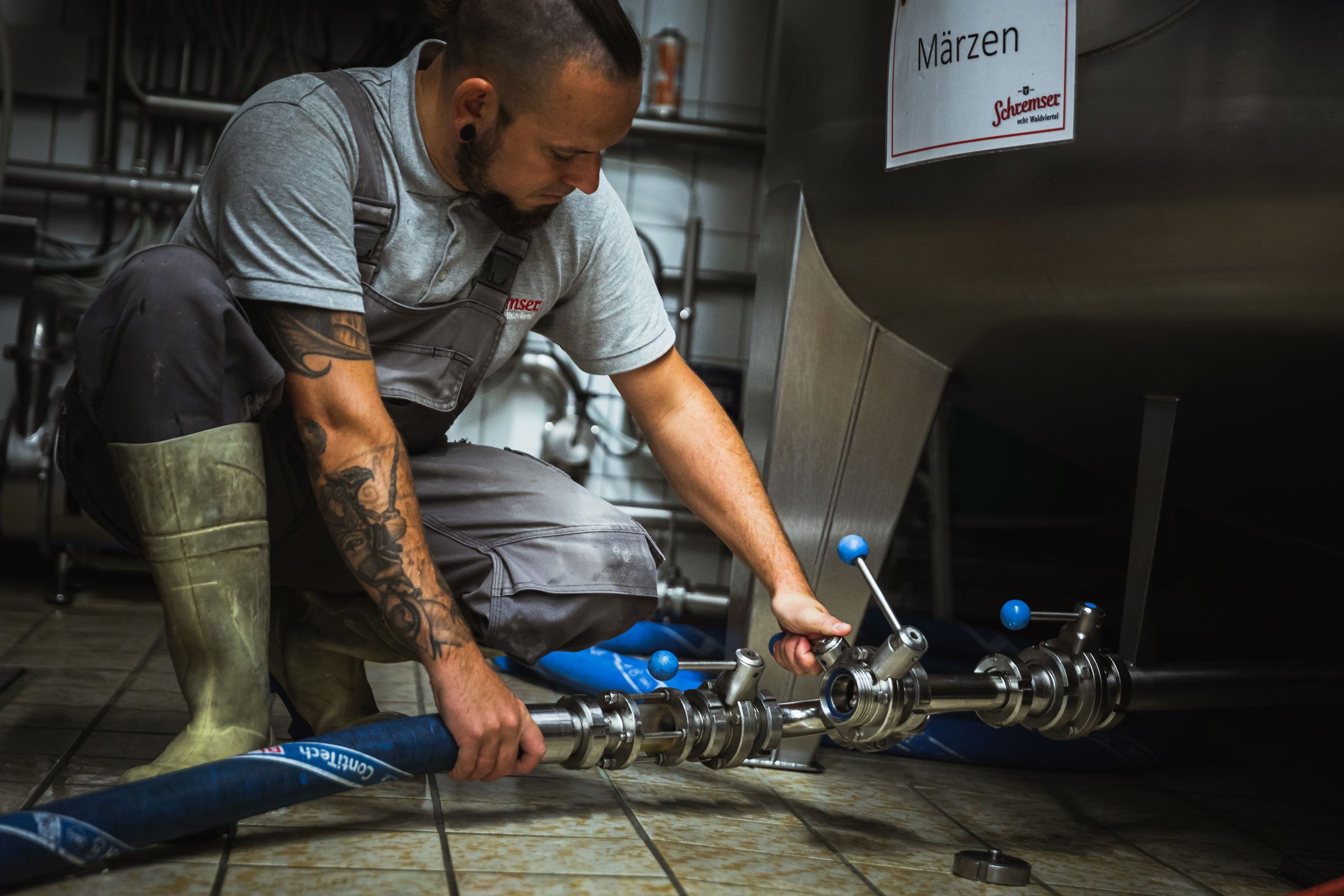 Ein Mann in Arbeitskleidung hält Biergläser vor einer Brauerei.