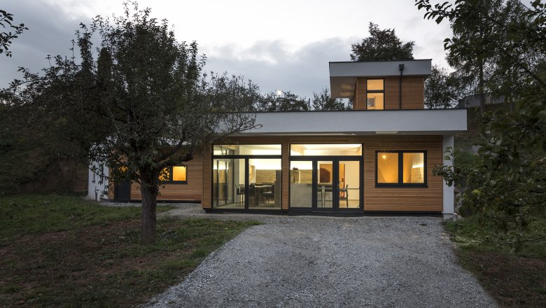 Au&szlig;enansicht einer modernen K&auml;serei mit gro&szlig;en Fenstern und Holzverkleidung, umgeben von B&auml;umen.