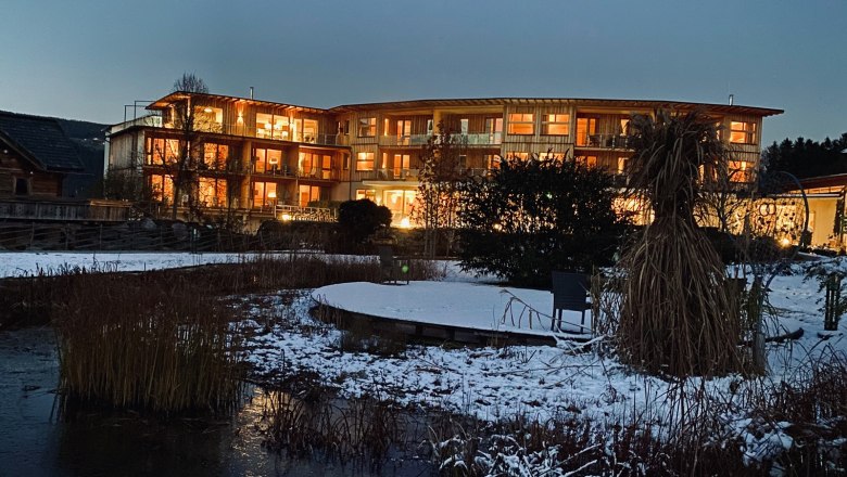 Beleuchtetes Geb&auml;ude bei Nacht mit verschneitem Garten im Vordergrund.