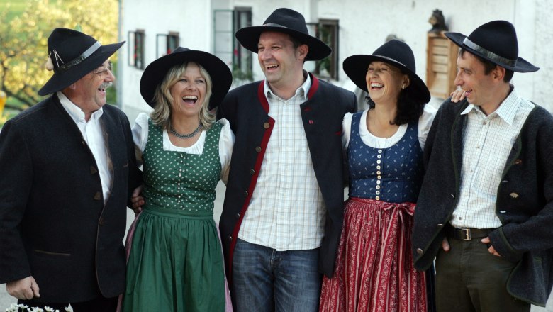 Gruppe von f&uuml;nf Personen in traditioneller bayerischer Tracht, die fr&ouml;hlich lachen.