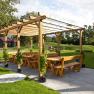 Holzpergola mit B&auml;nken und Tischen im Freien, umgeben von Rasen und B&auml;umen.