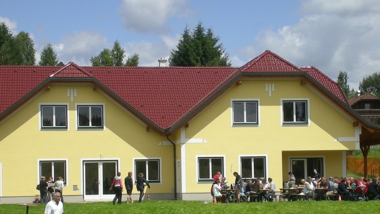 Gelbes Gebäude mit rotem Dach, Menschen sitzen draußen an Tischen.