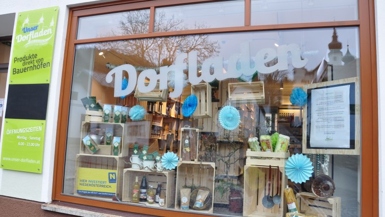 Schaufenster eines Dorfladens mit Produkten und Dekorationen.