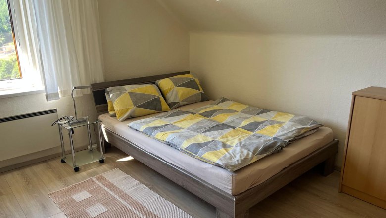 Ein gemütliches Schlafzimmer mit einem Doppelbett, gemusterten Bettbezügen, einem kleinen Nachttisch und einem Fenster mit Vorhängen.