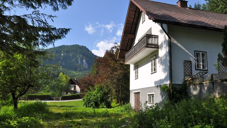 Ferienhaus Erlaufboden, © zVg Gemeinde Annaberg Ein weißes Ferienhaus mit Balkon vor einer Berglandschaft und grünem Garten.