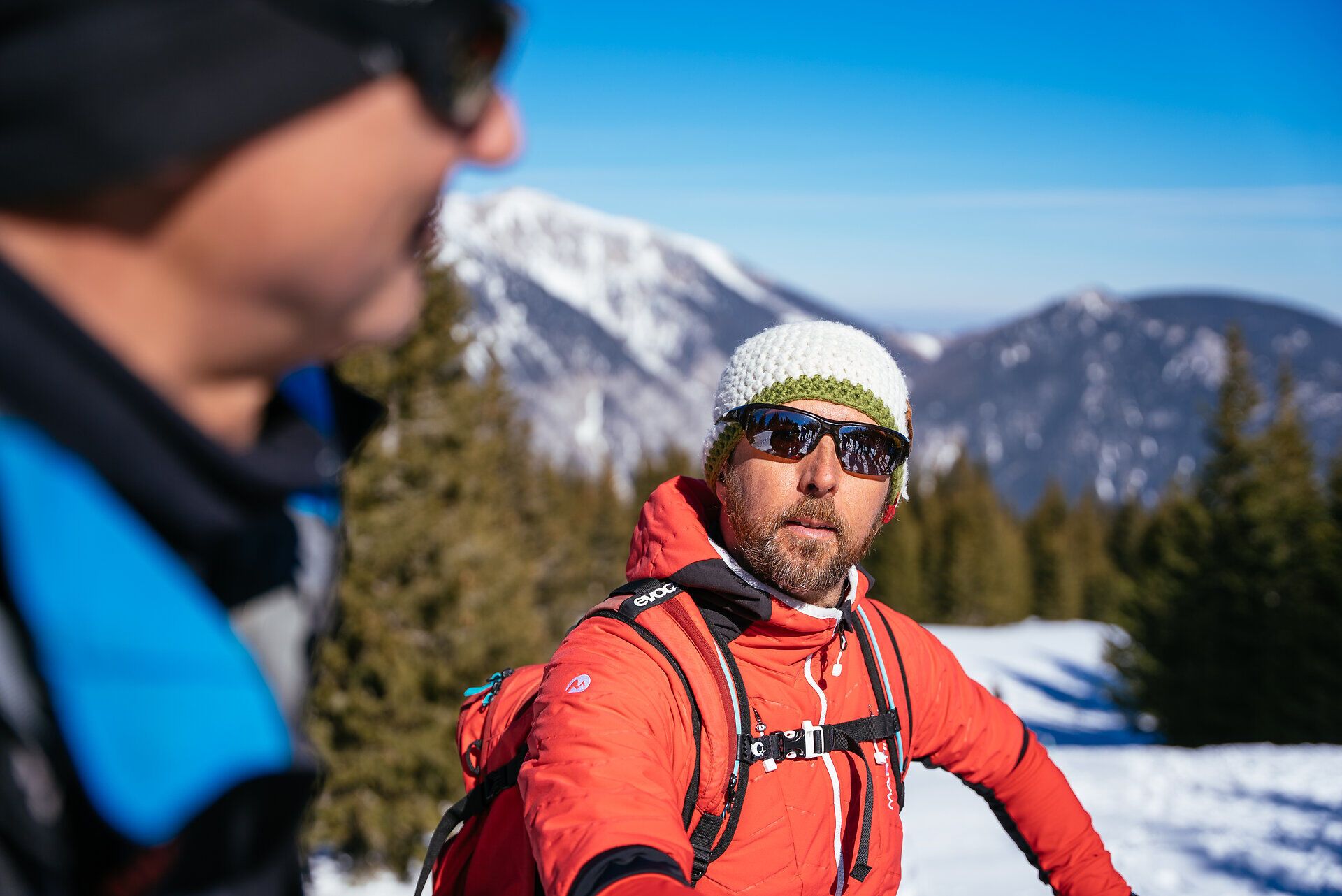 Wolfgang Menzel mit Gruppe von Menschen mit Schneeschuhen wandert auf verschneiter Fläche vor Nadelbäumen unter blauem Himmel