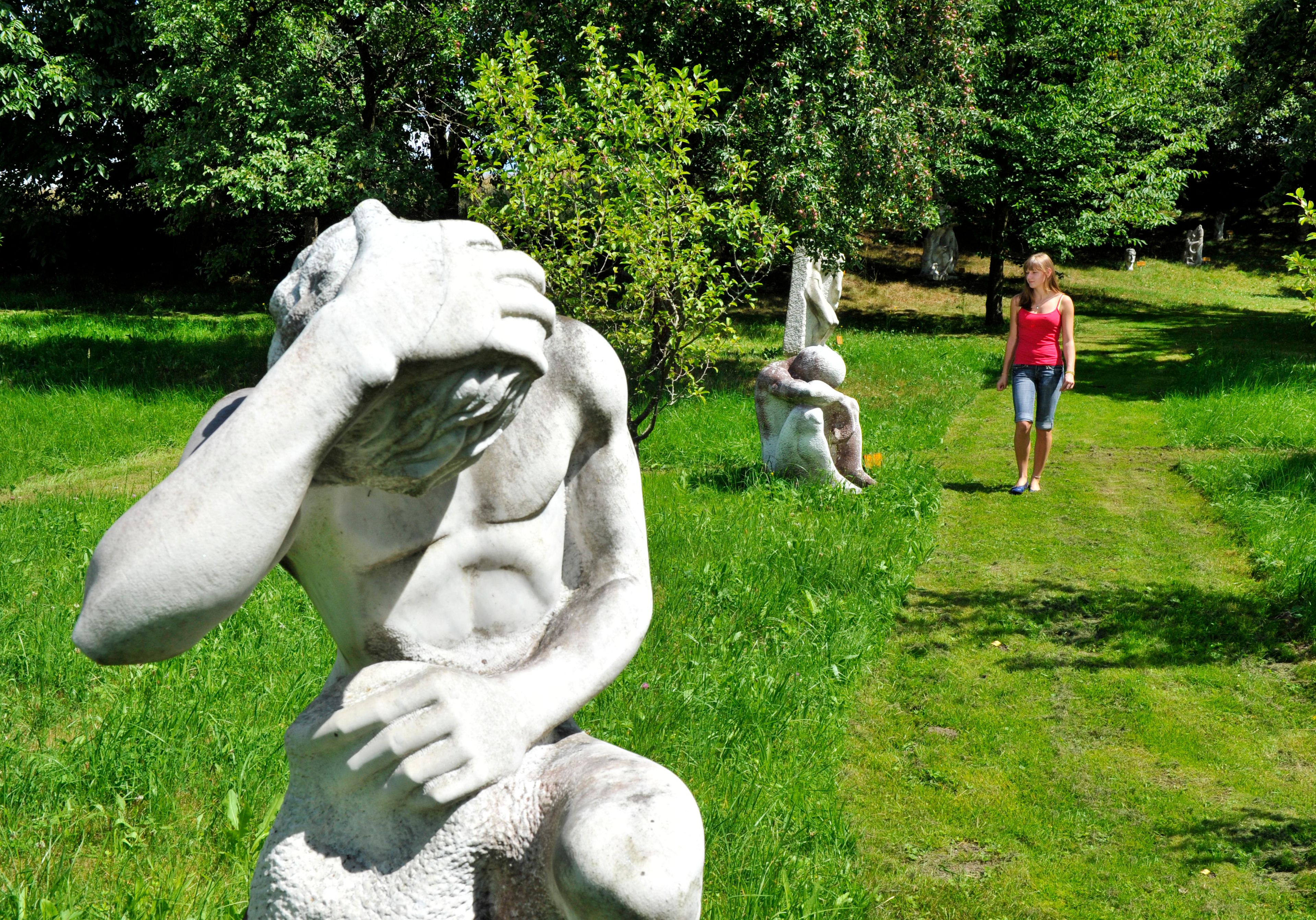 Eine Frau spaziert durch einen Garten mit mehreren Skulpturen auf einer grünen Wiese.