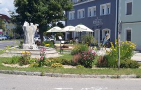 Außenansicht eines Cafés mit Garten und Skulptur.