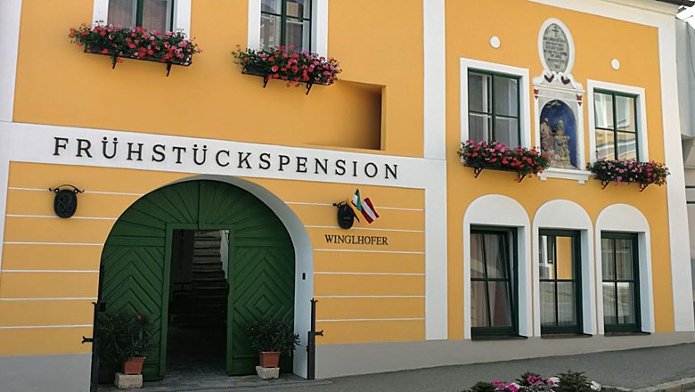 Gelbes G&auml;stehaus mit gr&uuml;ner T&uuml;r und Blumenk&auml;sten.