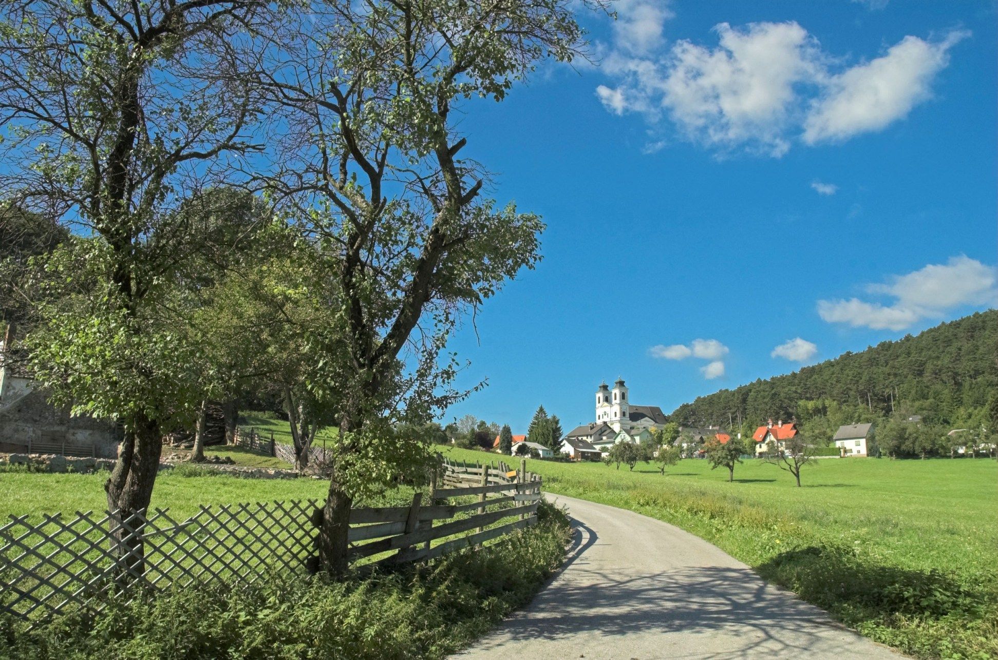Landschaft mit Kirche und Bäumen unter blauem Himmel.