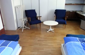 Ein Zimmer mit zwei blauen Sesseln, einem weißen runden Tisch und zwei Betten mit blauer Bettwäsche auf Holzboden.