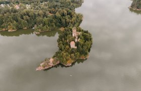 Luftaufnahme einer Burgruine auf einer bewaldeten Insel in einem See.