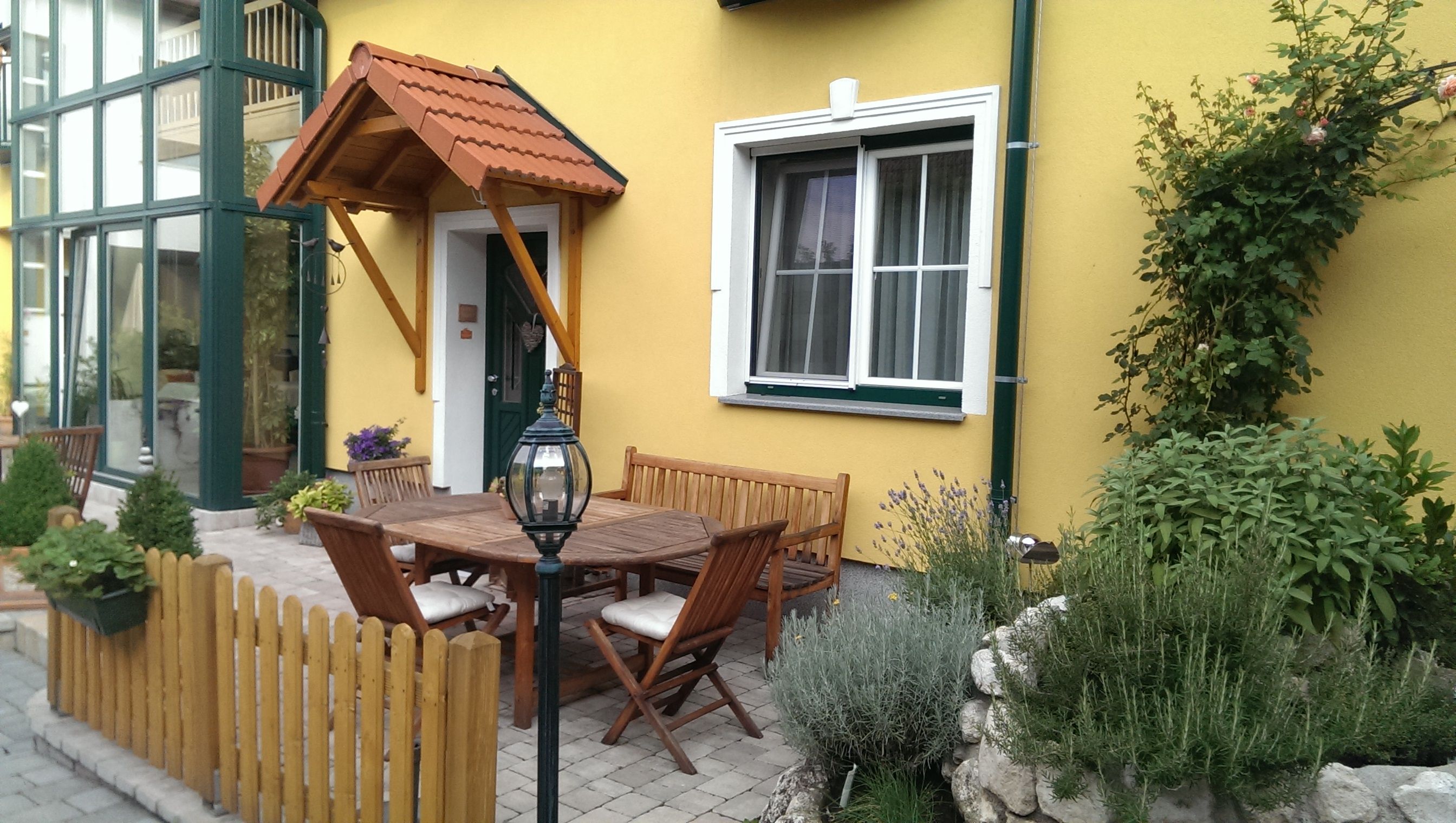 Ein gemütlicher Innenhof mit Holzmöbeln, Pflanzen und gelber Hausfassade.