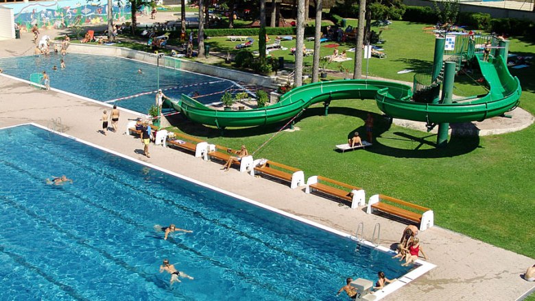 Ein Freibad mit zwei Schwimmbecken, einer gr&uuml;nen Wasserrutsche und Liegewiese.