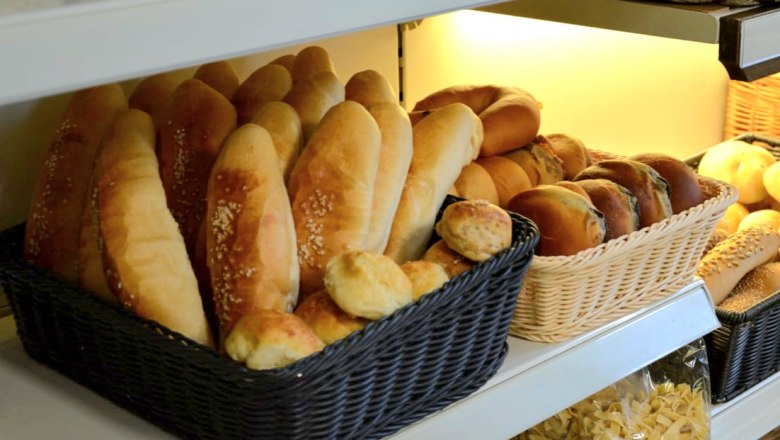 Regal mit verschiedenen Brotsorten in K&ouml;rben, darunter Baguettes und Br&ouml;tchen.